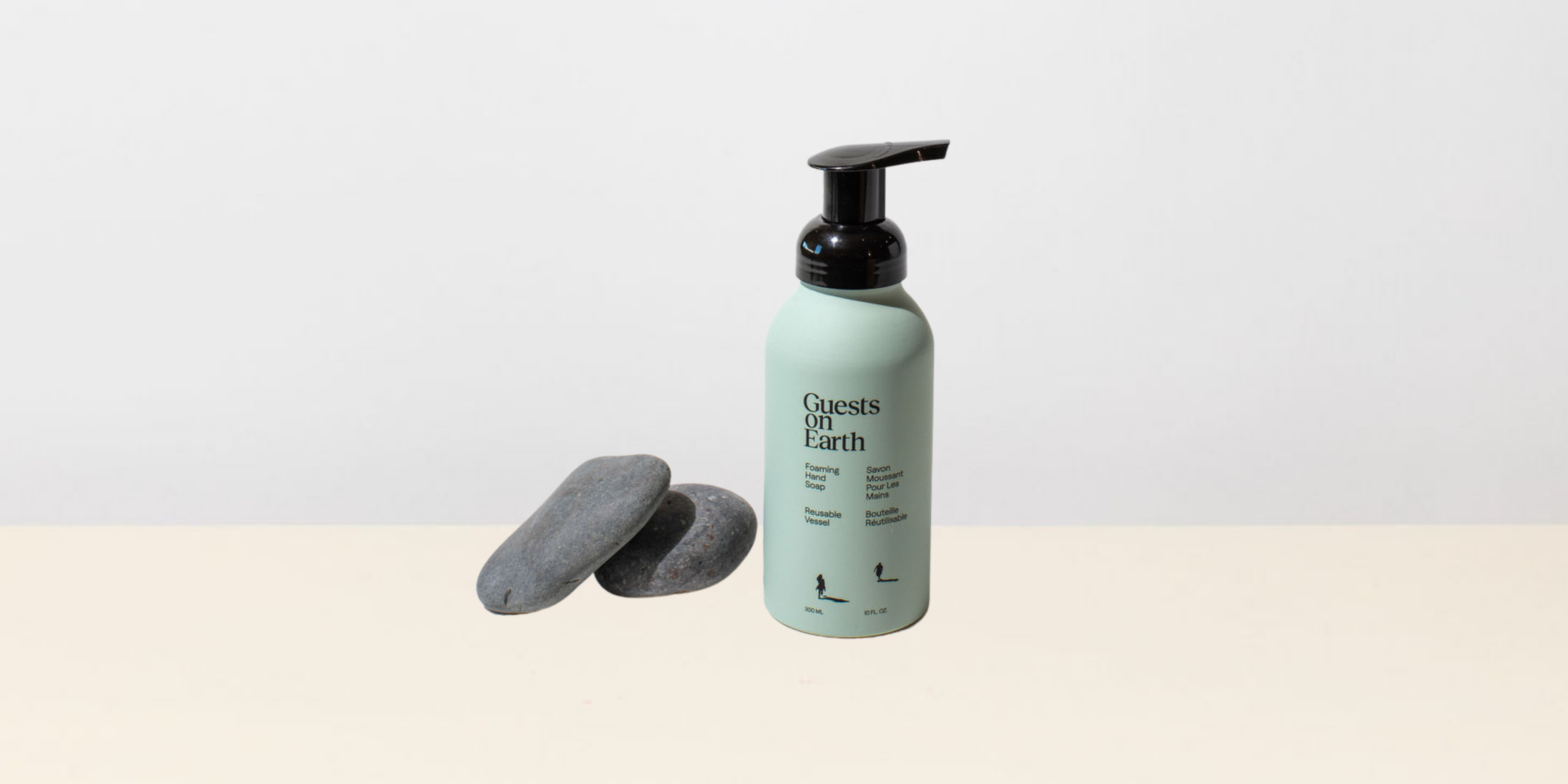 Reusable Guests on Earth foaming soap bottle next to stones