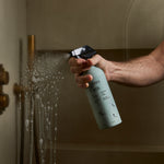 Guests on Earth All-Purpose Cleaner sprayed on a glass shower door, cutting soap scum with a refillable bottle