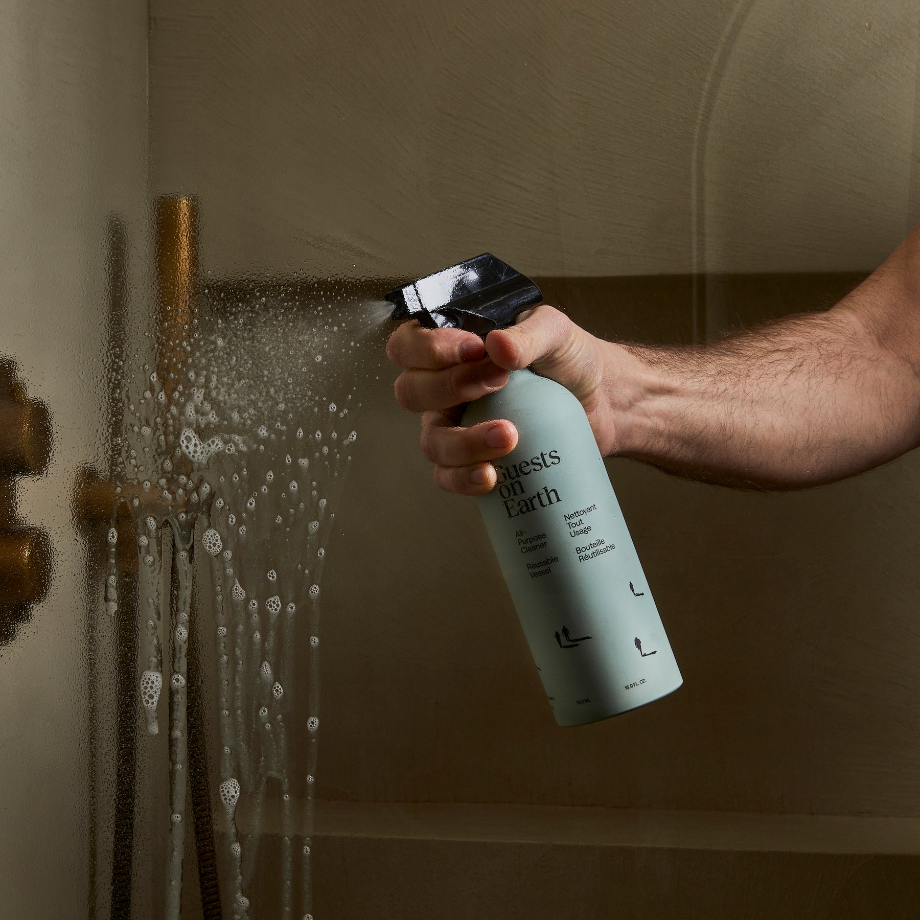 Hand sprays Guests on Earth bottle on shower glass, suds forming, cleaning for everyone