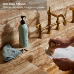 Guests on Earth Dish Soap & Brush at marble sink, bottle beside cloth as hands scrub a plate with a wooden brush