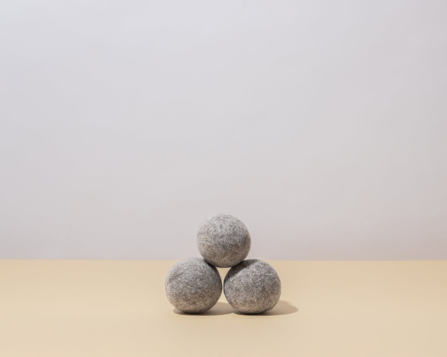 Guests on Earth Wool Dryer Balls, three grey felt balls stacked on a neutral surface in minimalist studio light