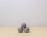 Guests on Earth Wool Dryer Balls, three grey felt balls stacked on a neutral surface in minimalist studio light