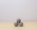 Guests on Earth Wool Dryer Balls, three grey felt balls stacked on a neutral surface in minimalist studio light