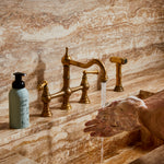 Guests on Earth Foaming Hand Soup by the sink as hands lather under a brass tap on a marble countertop