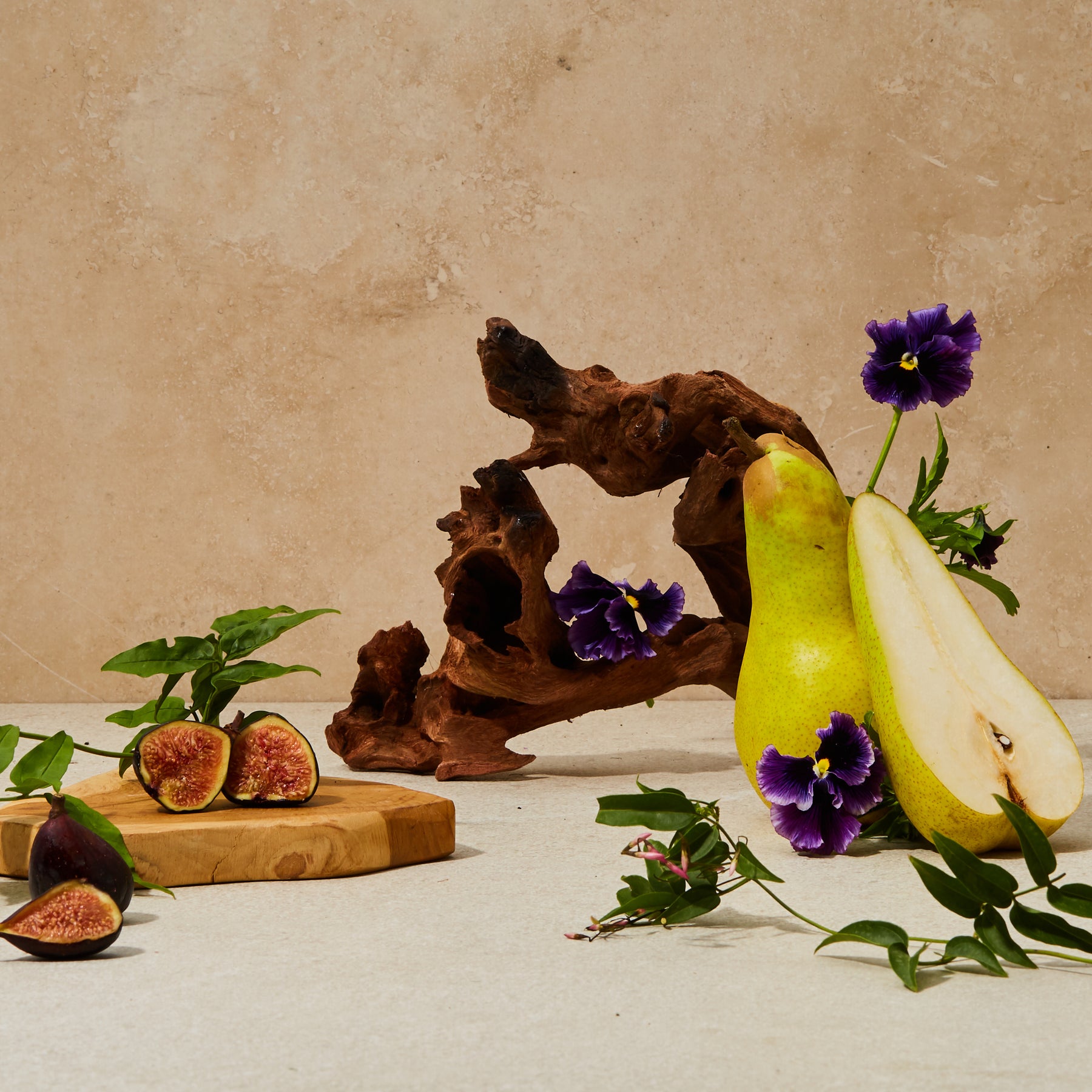 Guests on Earth Green Hinoki scent styled with pears, figs, purple flowers, and sculptural wood