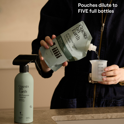 Guests on Earth refill pouch pours cleaner concentrate into a measuring cup beside a reusable spray bottle.