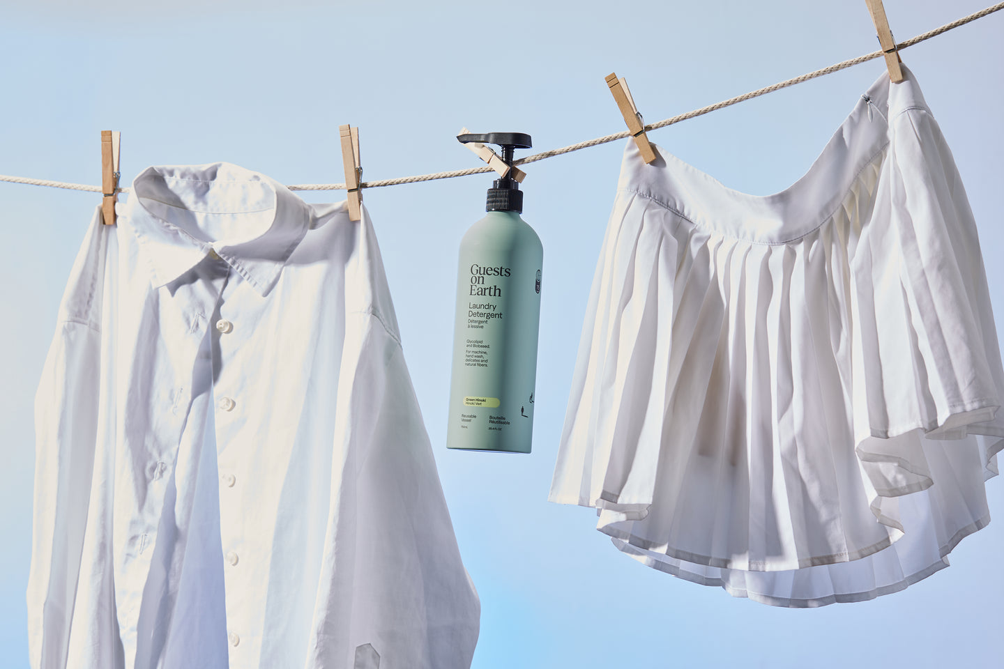 Guests on Earth Laundry Detergent bottle hangs on a clothesline between crisp white shirt and skirt in daylight