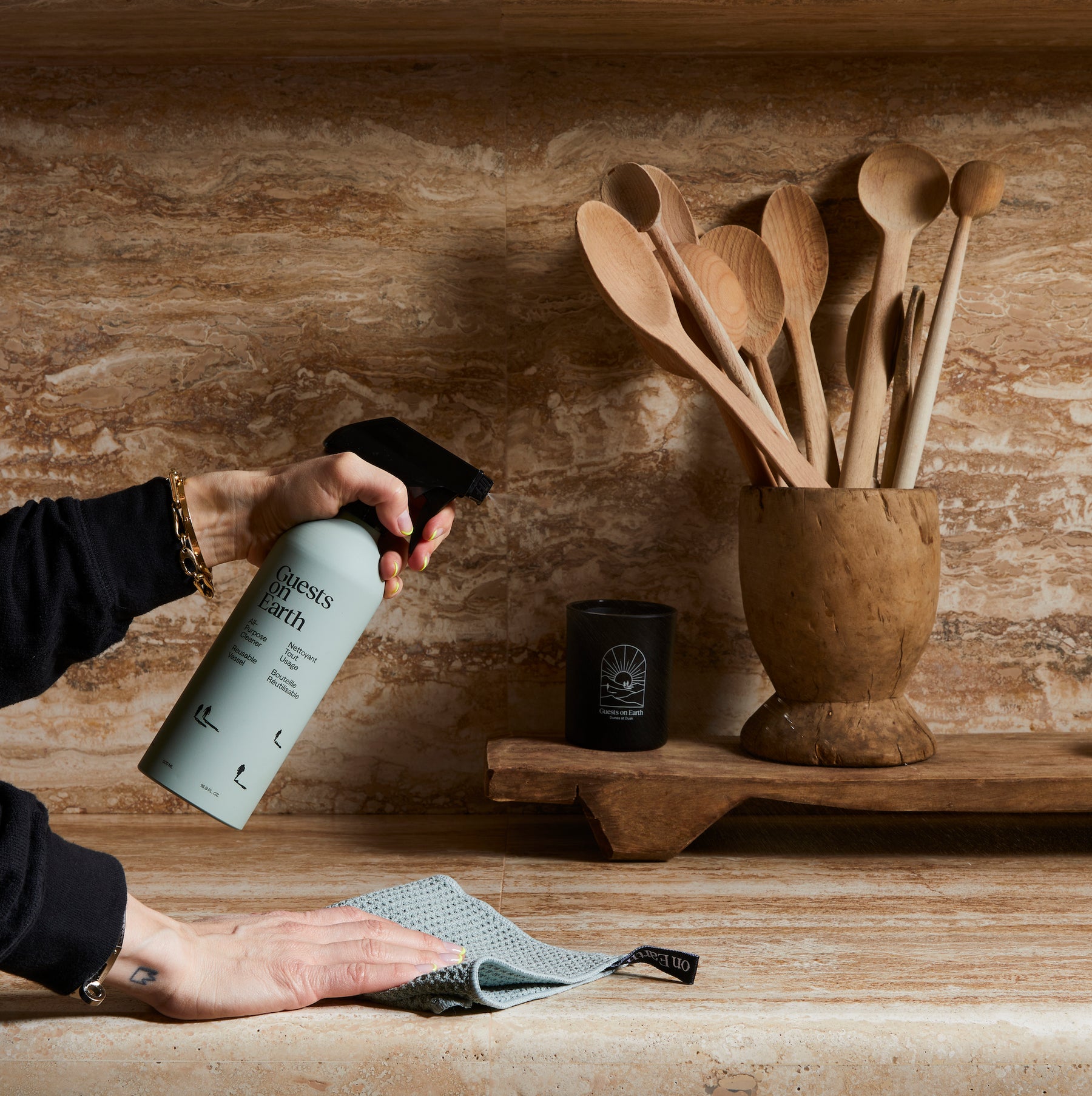Guests on Earth All-Purpose Cleaner sprayed on kitchen counter as cloth wipes near wooden utensils