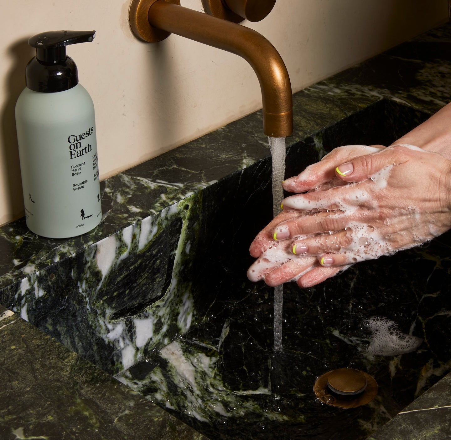 Guests on Earth Foaming Hand Soap beside marble sink as hands lather under running water